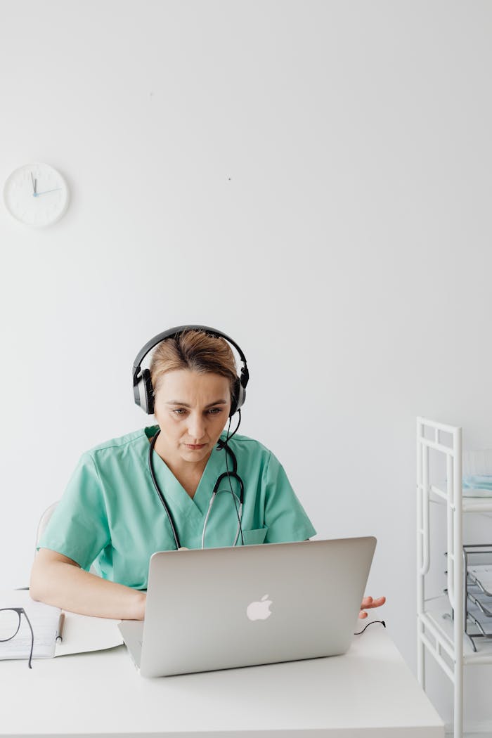 Female doctor wearing headphones conducting online consultation on a laptop in a clinical setting.