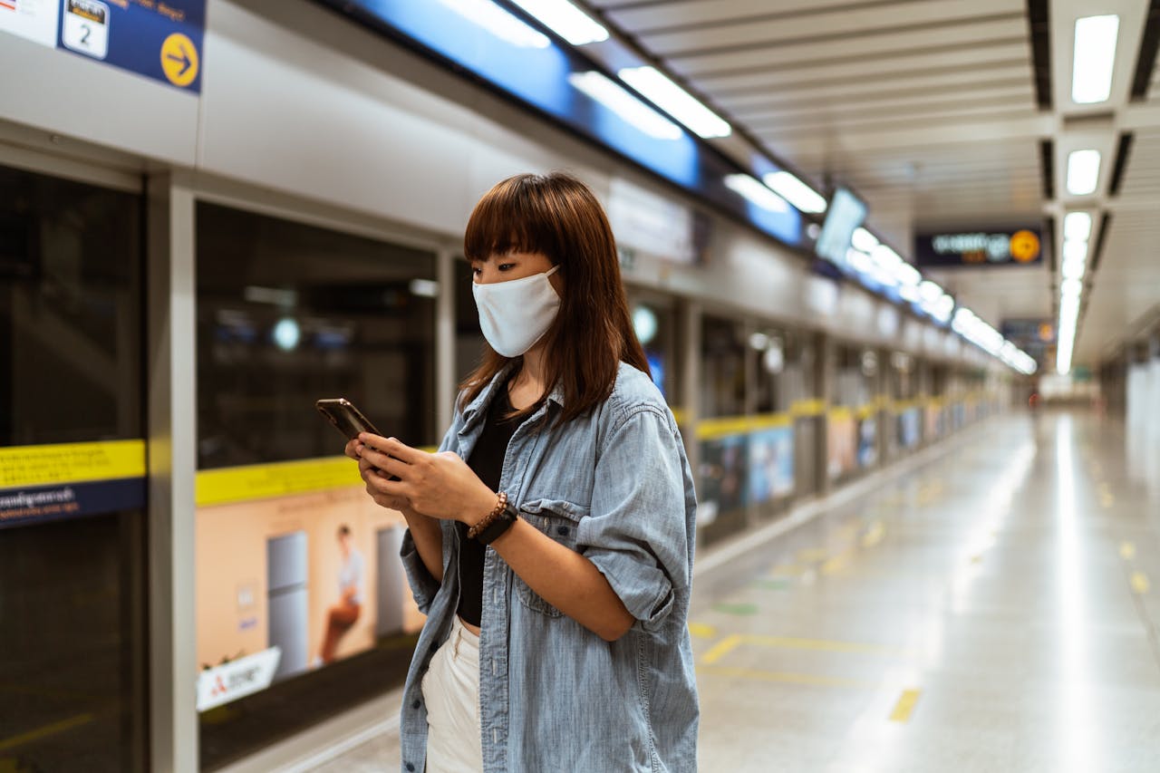 Young woman in a face mask using a smartphone at an empty subway station.